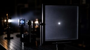 Frosted detector plate showing one bright measurement point in a dark optics lab